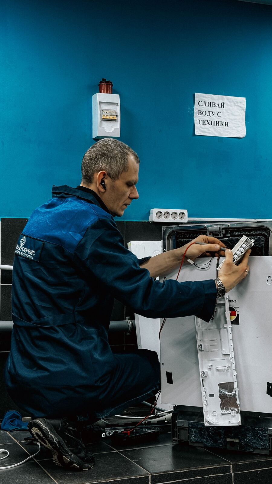 Technician testing a built-in dishwasher control panel with multimeter probes