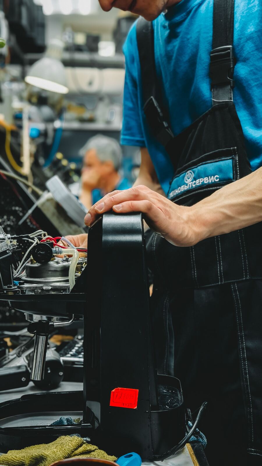 Technician holding an espresso machine with the housing off to show its boiler and hoses