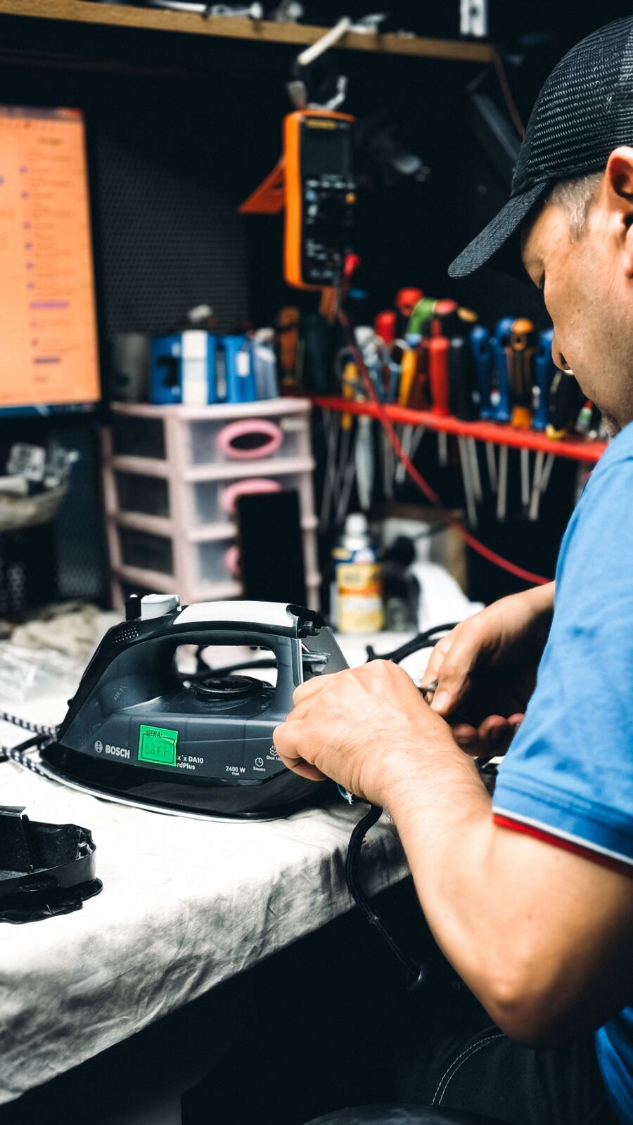 Technician working on the power cord connection of a steam iron at the bench