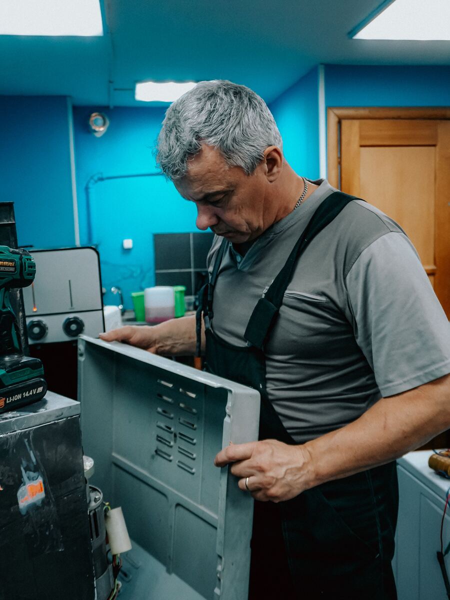 Technician removing a metal cabinet panel from a large laundry appliance